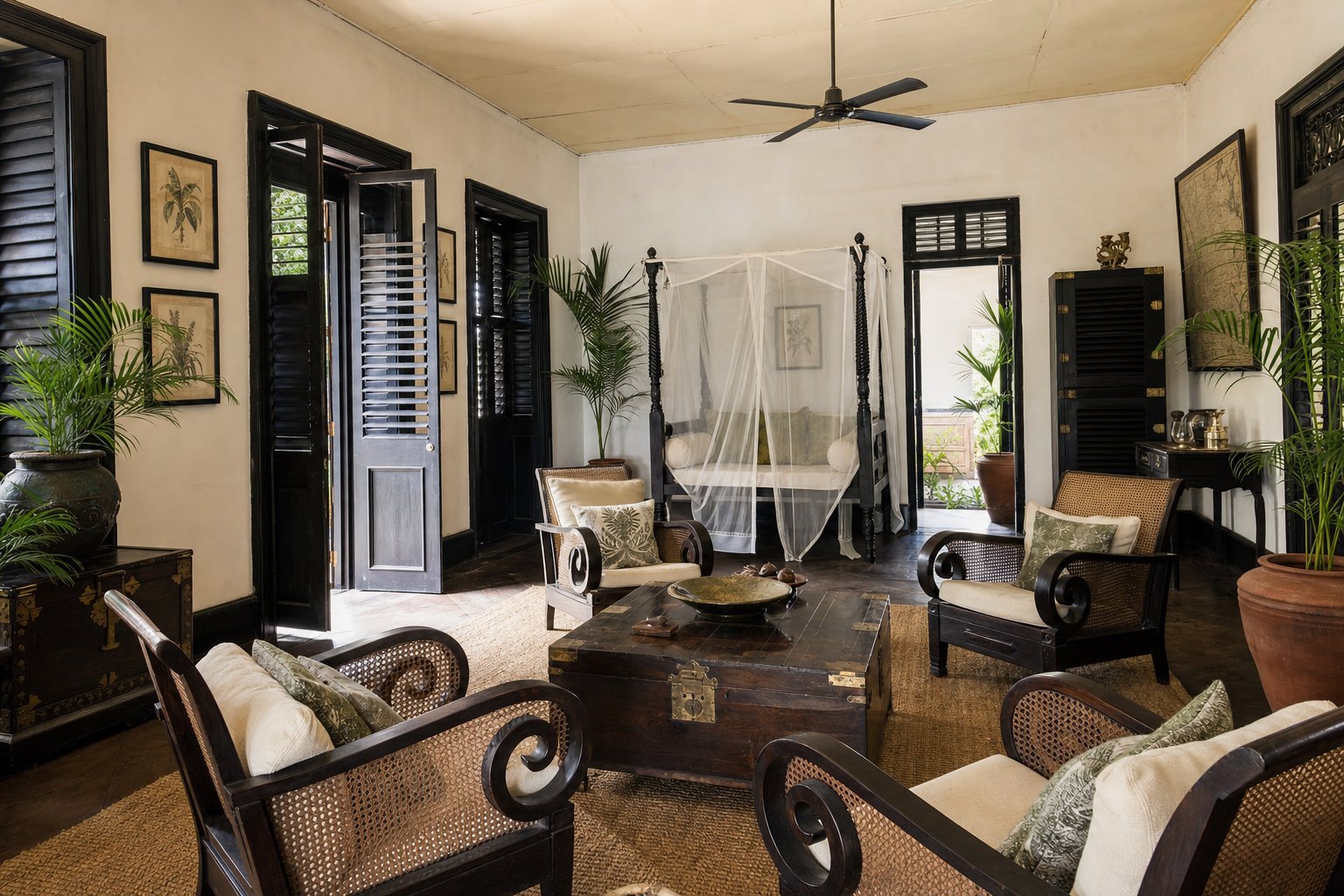 British Colonial room with dark hardwood furniture, pale walls, cane seating, shutters, a ceiling fan, and tropical plants